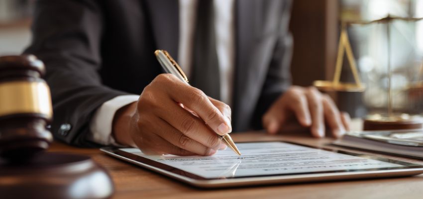 Lawyer reviewing and signing a valid contract on a tablet with legal scales and gavel nearby.