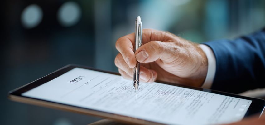 Business professional using a stylus to electronically sign a legal document on a tablet, illustrating the acceptance element of contract formation