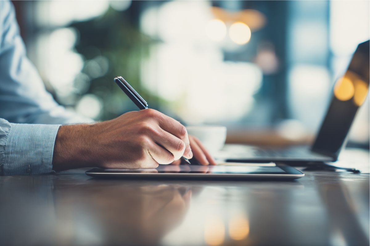 A business professional signs a contract addendum on a digital tablet using a stylus at a modern workspace